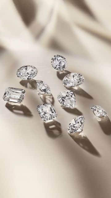 Sparkling diamonds of various cuts on a soft beige surface, casting elegant shadows.