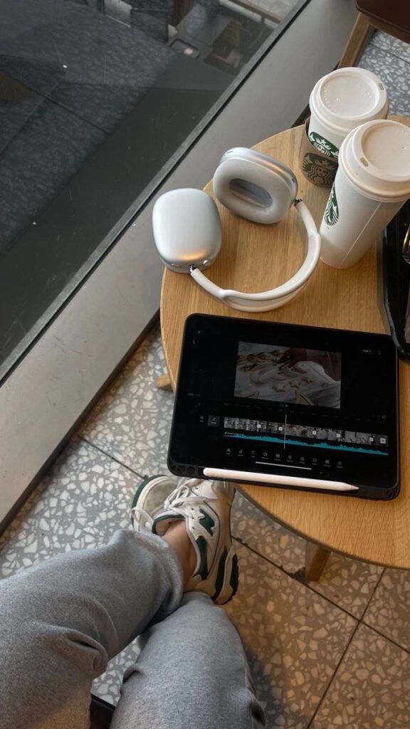 Person editing video on tablet with headphones and coffee in a cafe setting.