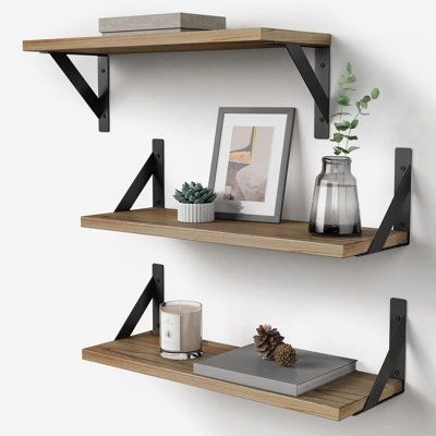 Wall-mounted wooden shelves with black brackets, decorated with books, plants, candles, and a framed photo.
