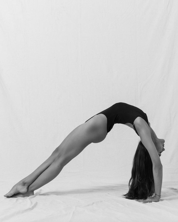 Woman performing a bridge pose in a leotard, showcasing flexibility and strength on a white background.