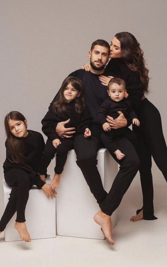 Family portrait with parents and three children wearing matching black outfits, posing together affectionately.