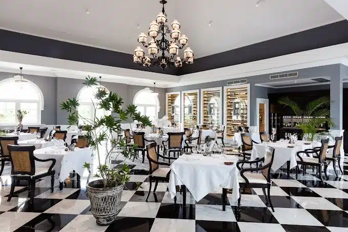 Elegant restaurant interior with classic black and white checkered floor, chandeliers, and neatly set tables with white linens.