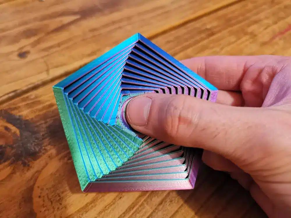 Colorful fidget toy in hand, featuring a twisted geometric design on a wooden table.