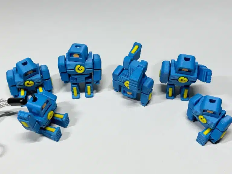 2024-06-04_b6f5c2c1cece1 Six small blue robot toys with yellow details posed on a white surface. | Sky Rye Design Six small blue robot toys with yellow details posed on a white surface.