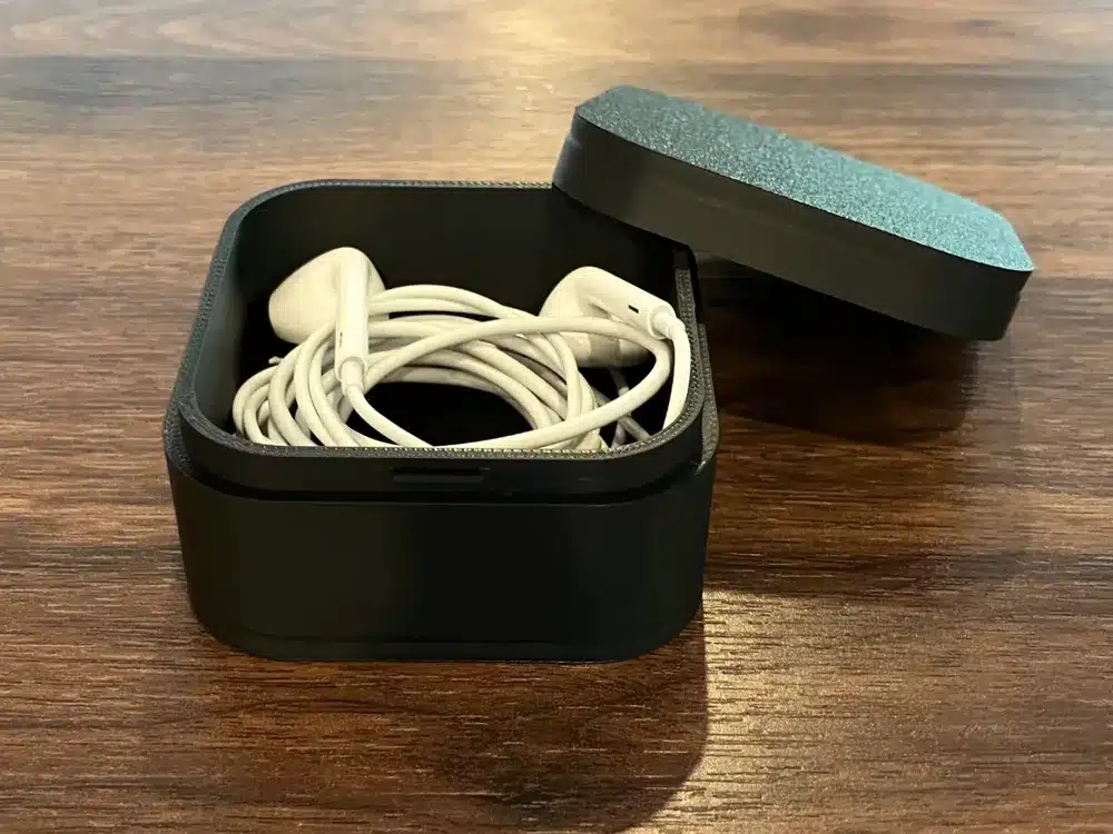 White earphones neatly stored in a black open case on a wooden surface.