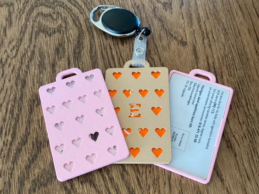 Pink and beige heart-patterned cardholders with a keychain on a wooden surface.