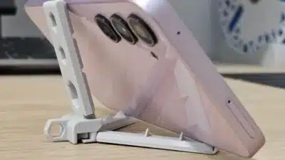 Smartphone on a desk in a white stand, showcasing camera lenses and durable case in a tech setting.