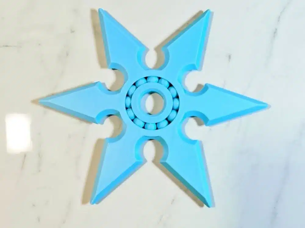 Blue fidget spinner shaped like a shuriken on a marble surface.