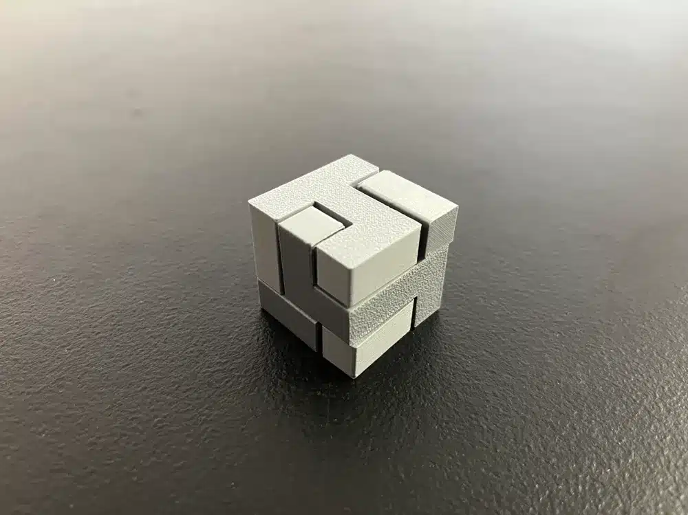 Gray interlocking metal puzzle cube on a dark surface.