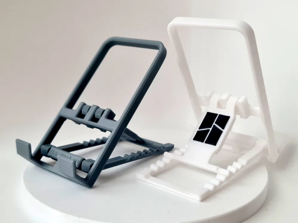Two 3D-printed mobile stands, one gray and one white, displayed on a round platform.