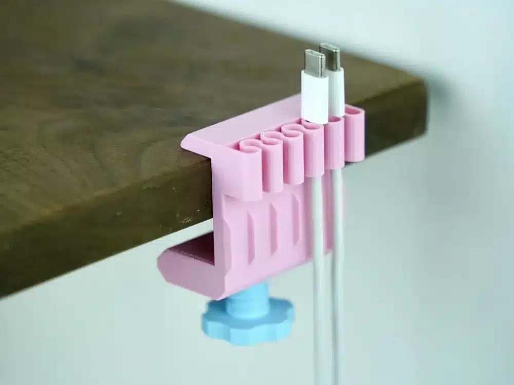 Pink desk cable organizer securing two cables on a wooden table edge for neat cord management.