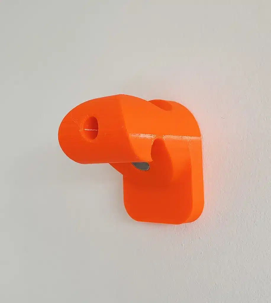 Bright orange 3D-printed hook on a wall, minimal design for efficient storage and organization.