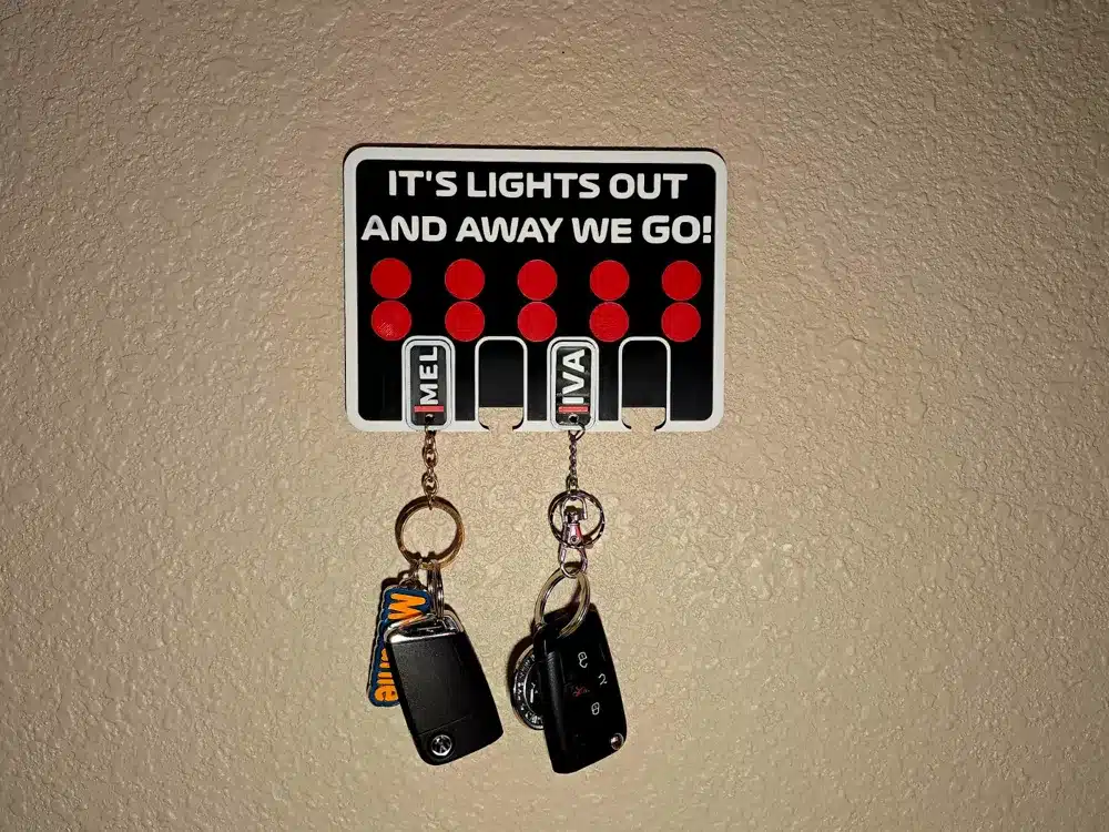 Wall-mounted key holder with It's lights out and away we go! design, holding two sets of car keys.