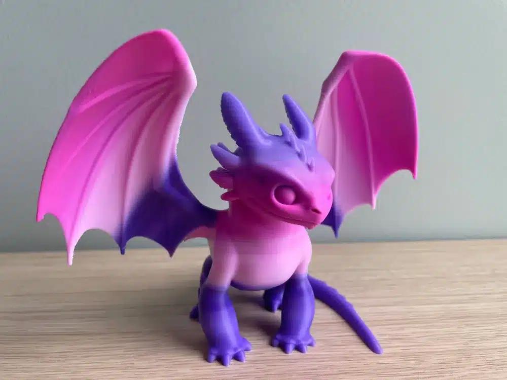 Colorful dragon figurine with pink and purple hues on a wooden surface.