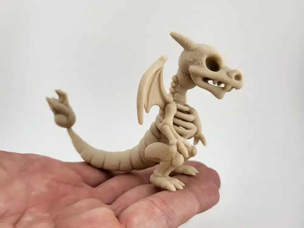 A small 3D-printed dragon skeleton model held in a hand, showcasing intricate details on a light background.