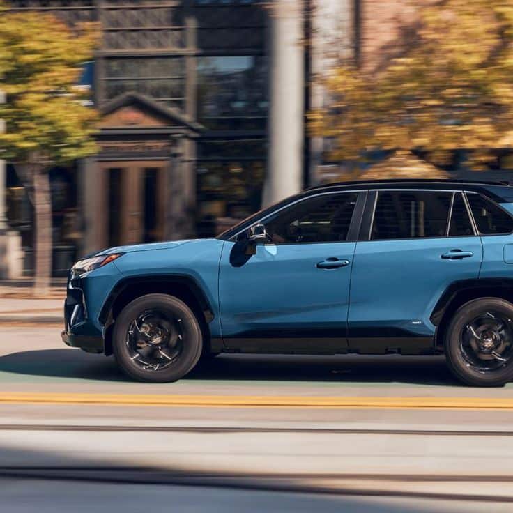 Blue SUV driving through city streets with blurred background and autumn trees.