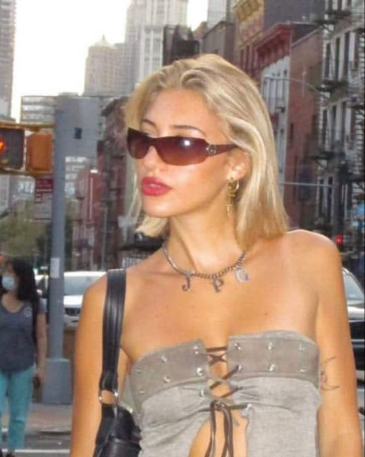 Stylish woman in sunglasses and a strapless top walking in an urban setting with skyscrapers in the background.