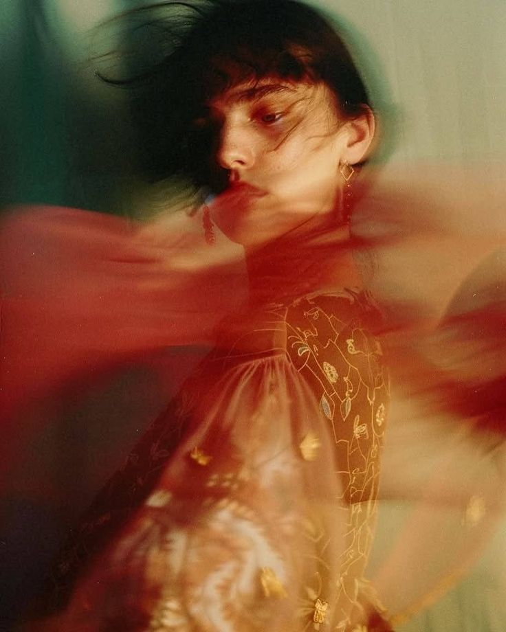Artistic portrait of a person in motion, wearing a colorful, embroidered outfit against a dreamy, blurred backdrop.
