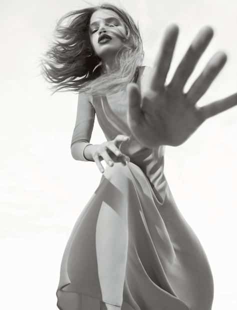 Woman in flowing dress reaching towards camera, dynamic black and white fashion shot.