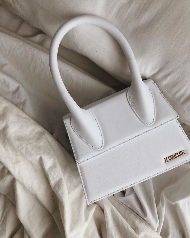 Elegant white handbag with curved handles on soft fabric background, featuring gold brand logo accent.