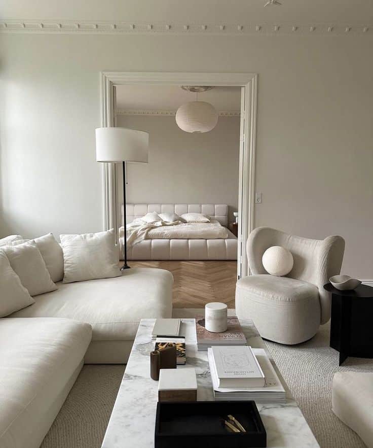 Modern minimalist living room with neutral tones, cozy seating, marble coffee table, and view into a stylish bedroom.