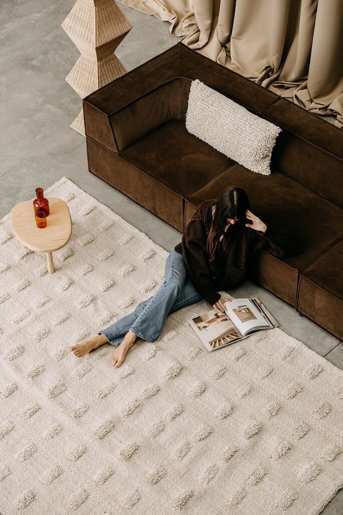 Woman reading on cozy rug with brown sofa and modern decor, enhancing serene living room ambiance.