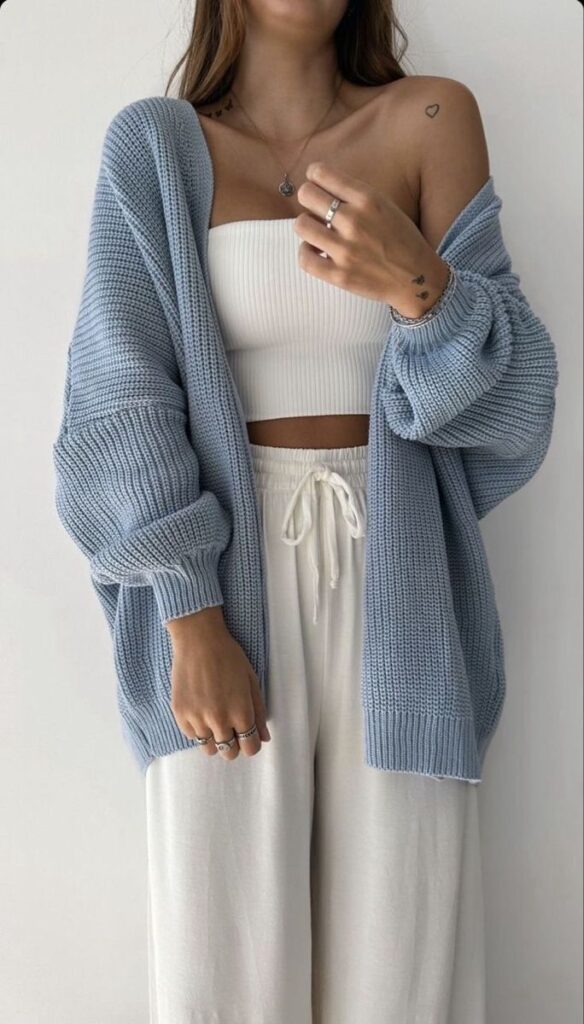 Woman in cozy blue cardigan and casual outfit, showcasing minimalistic style with a heart tattoo and jewelry accents.