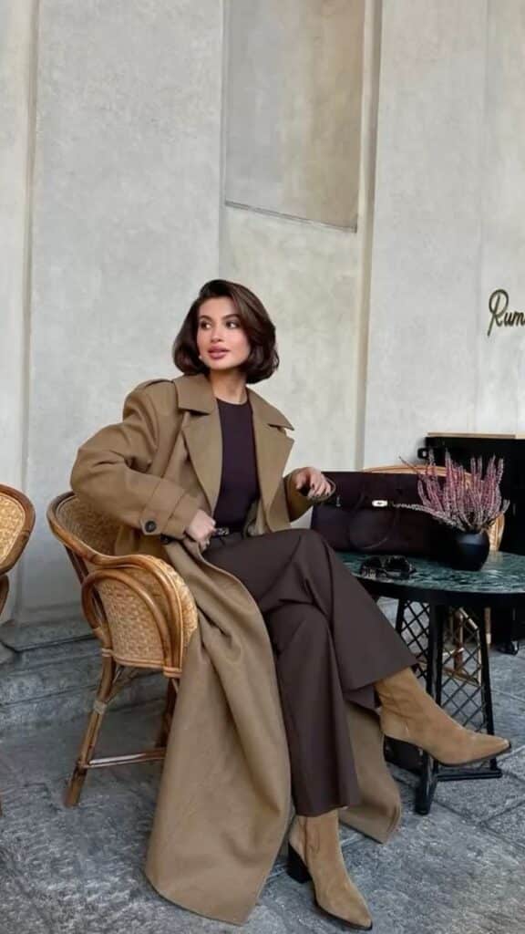 Woman in a stylish brown coat sitting in a cafe, exuding elegance and sophistication.