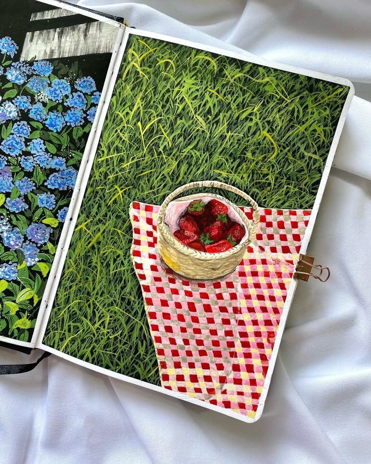 Illustrated notebook page with strawberries on a checkered cloth in grass, next to blue flowers.
