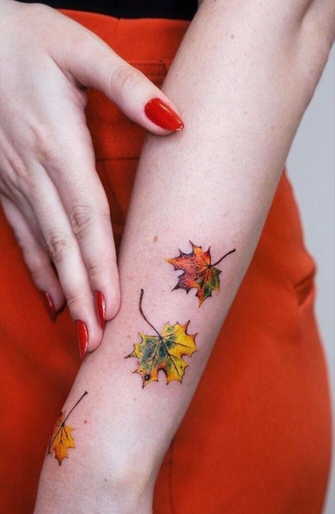 Realistic autumn leaf tattoos on forearm; vibrant fall colors; elegant red nails.