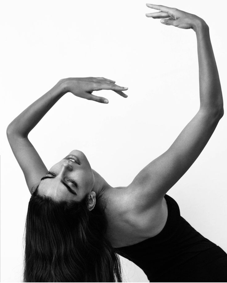 Graceful dancer arching back in an elegant pose with arms raised against a white background. Black and white photography.