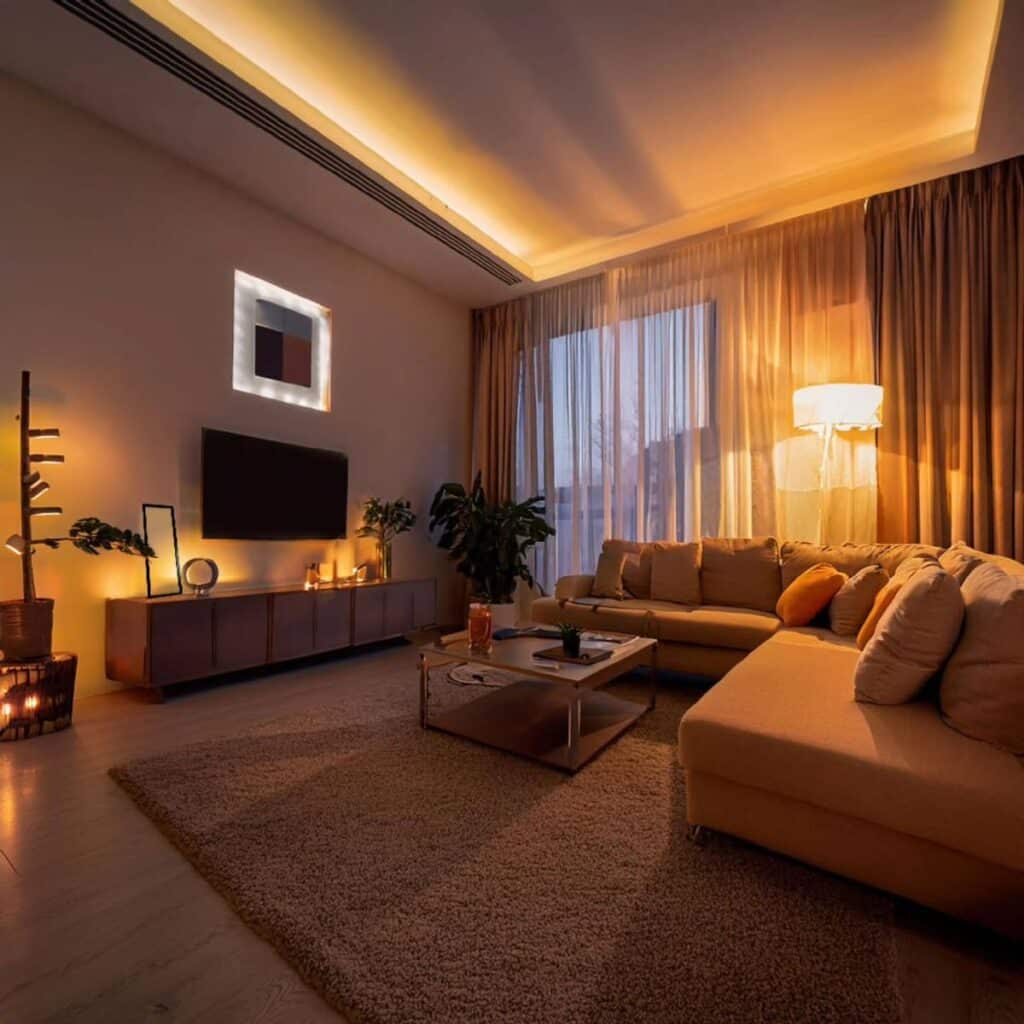 Cozy living room with modern lighting, sectional sofa, and large windows for a warm, inviting atmosphere.