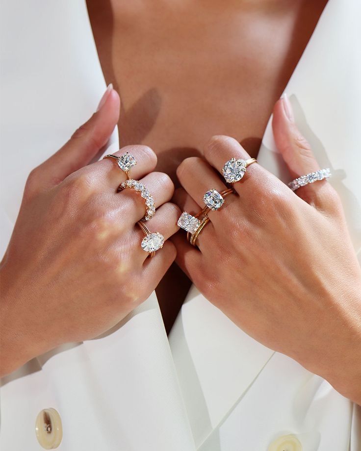 Close-up of hands showcasing multiple diamond rings on fingers over a white blazer. Luxurious jewelry display.