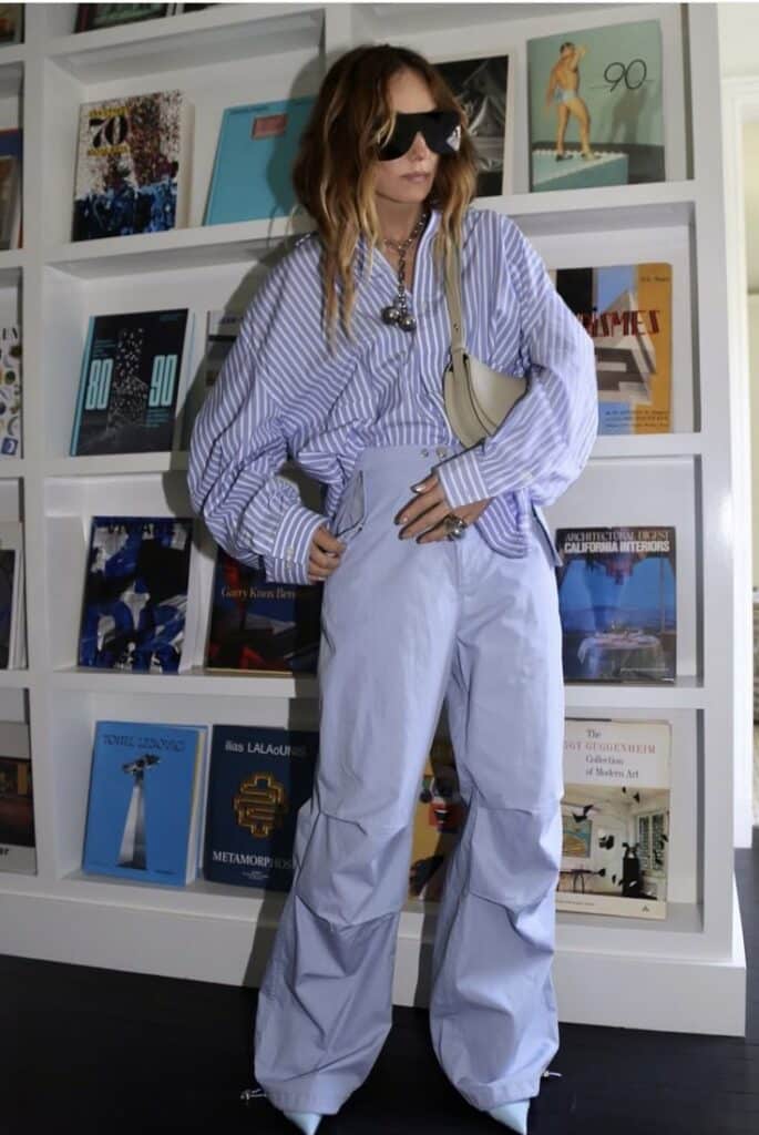 Screenshot Fashionable woman in oversized striped shirt and pants, wearing sunglasses, posing stylishly in front of bookshelf. | Sky Rye Design Fashionable woman in oversized striped shirt and pants, wearing sunglasses, posing stylishly in front of bookshelf.