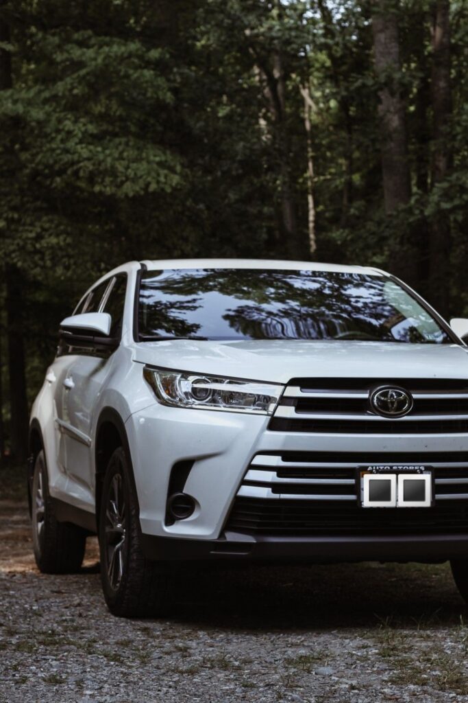 White SUV parked on gravel road in forest, showcasing sleek front grille and headlights.