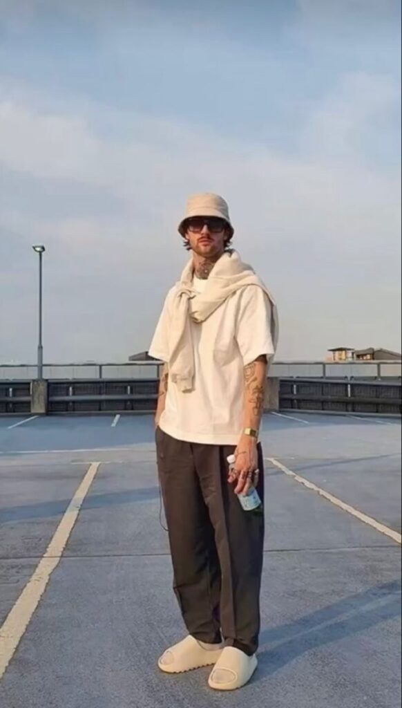 Man in casual outfit with bucket hat and sunglasses standing on rooftop parking lot.