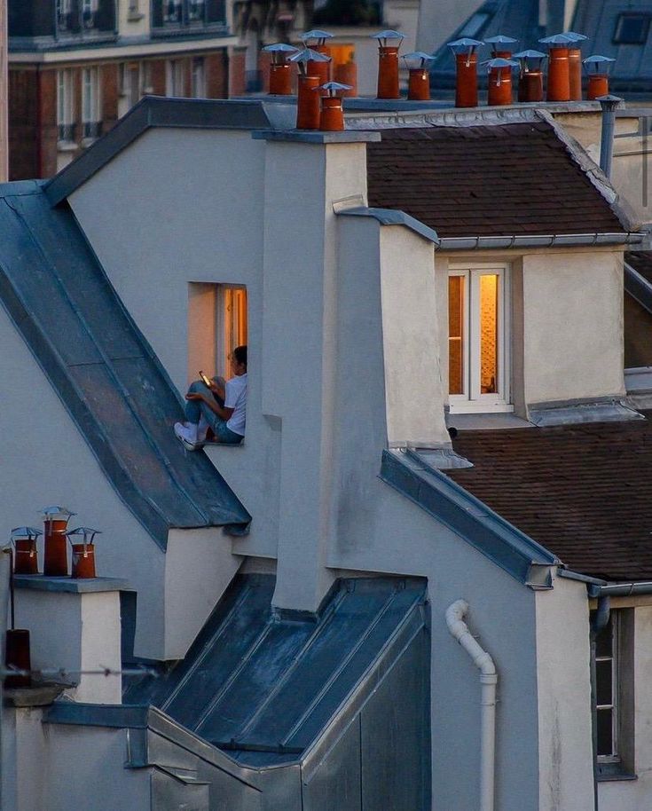 Person sitting by a window on a rooftop, view of urban architecture at twilight.