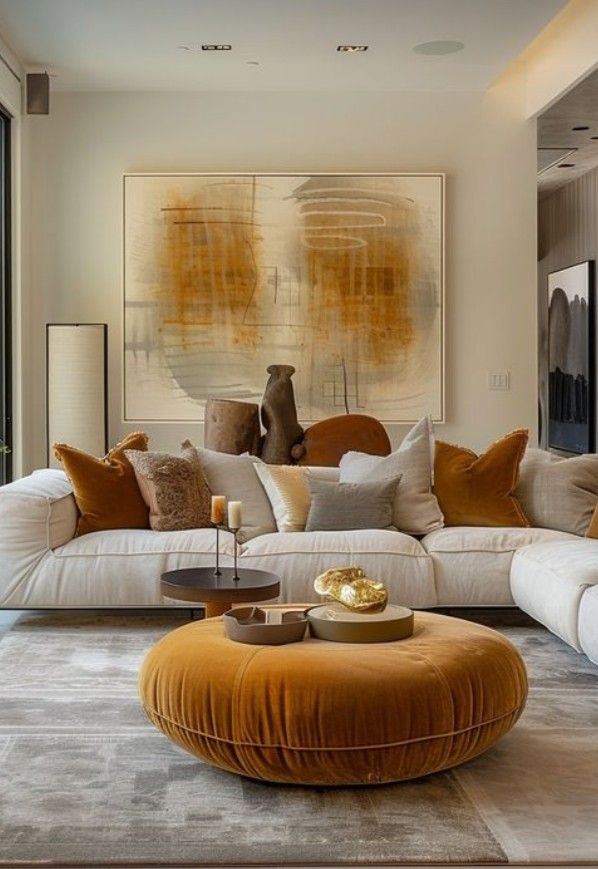 Modern living room with abstract art, mustard ottoman, white sofa, and decorative pillows for a cozy ambiance.