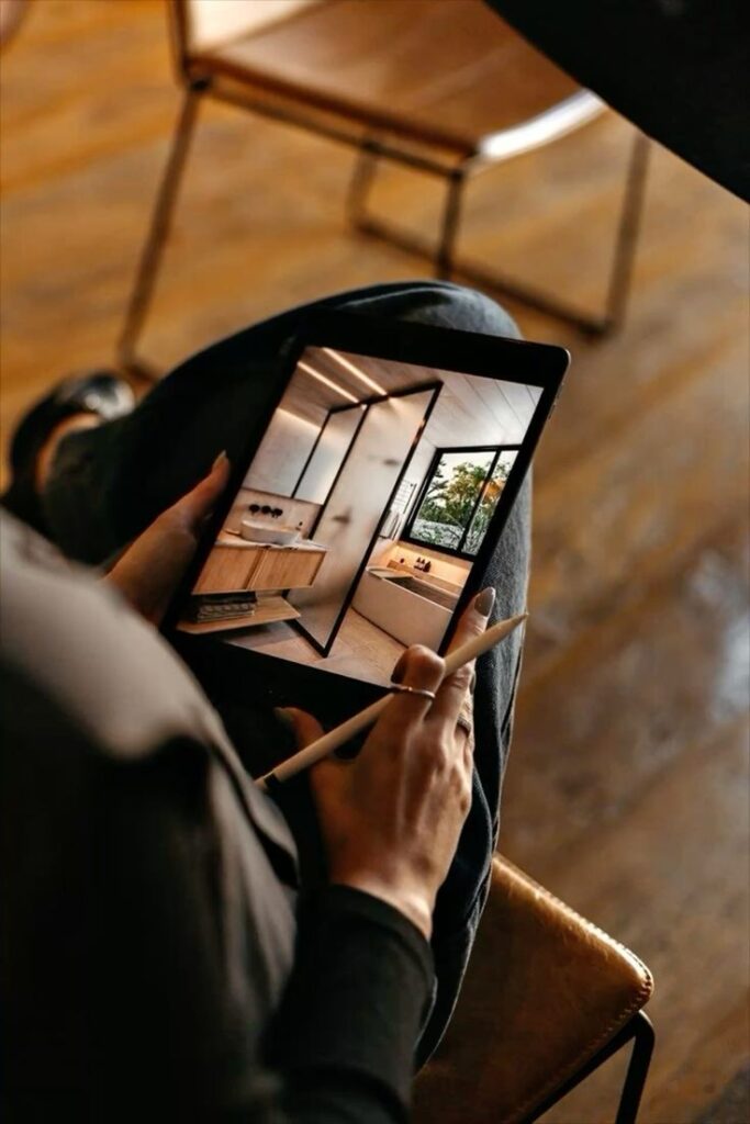 Person using stylus on tablet with interior design displayed, sitting on a chair.
