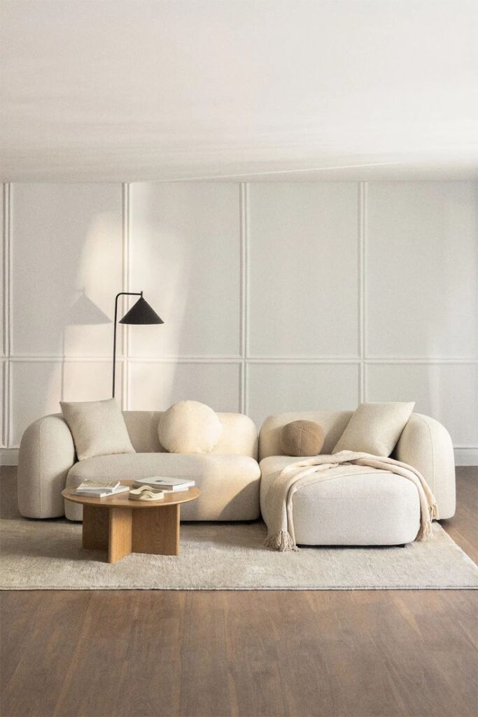 Modern beige living room with cozy sofa, round coffee table, and stylish floor lamp on wooden floor.