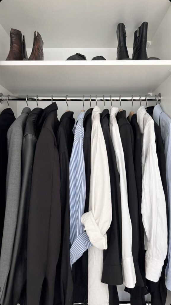 Wardrobe with neatly organized shirts and jackets, boots above, showcasing minimalist clothing style.