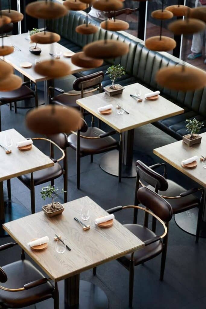 Modern restaurant interior with wooden tables, green booths, and elegant table settings.