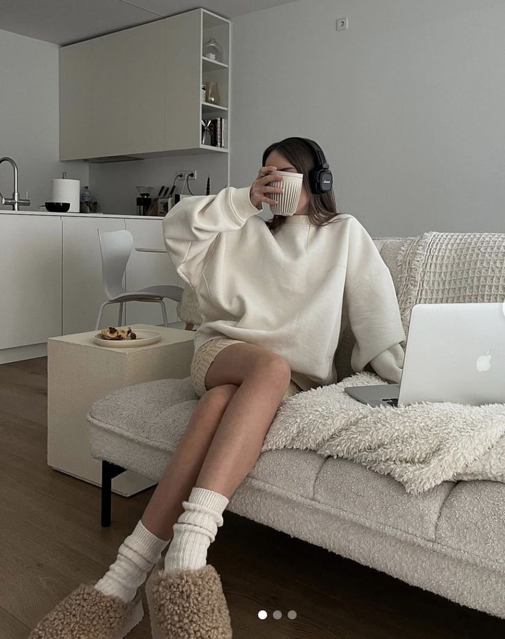 Cozy home office setup: person on sofa with laptop, coffee, and headphones in minimalist living room.