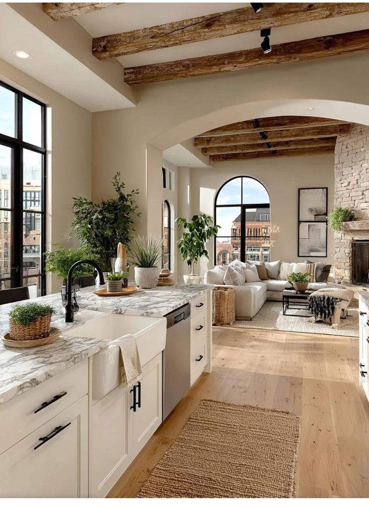 Modern open-concept kitchen and living room with wooden beams, marble countertops, and large windows.