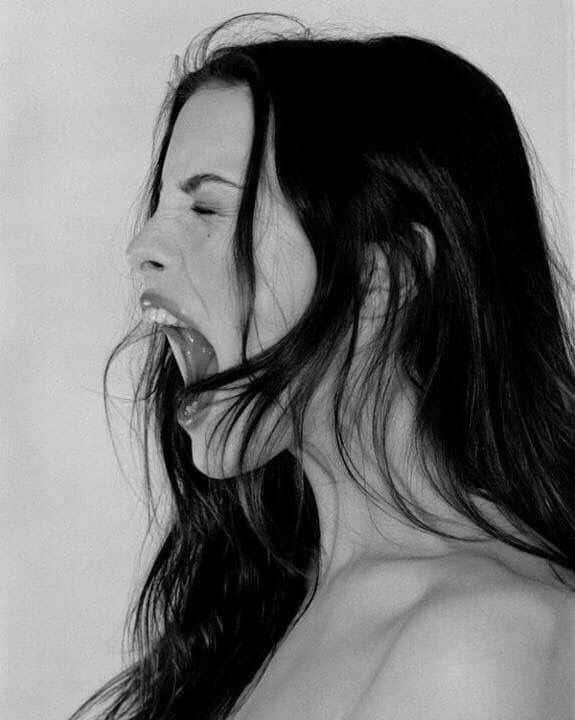 Black and white photo of a woman with long hair passionately shouting, expressing emotion and intensity.