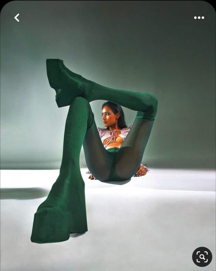 Fashion model in green bodysuit poses artistically with dramatic lighting and shadow, showcasing unique style and flexibility.