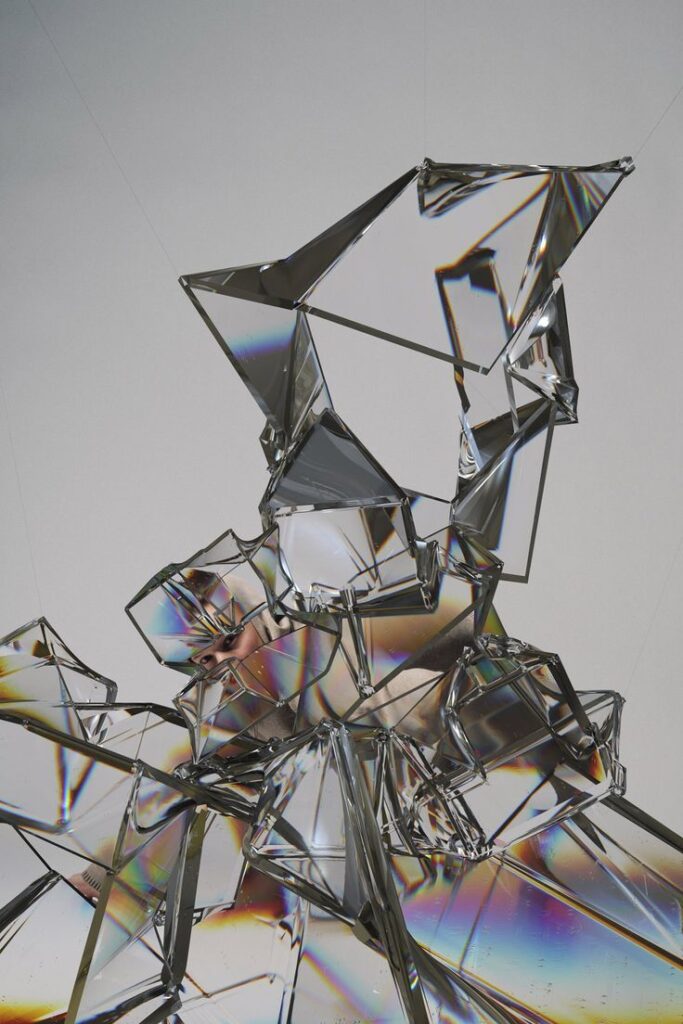 Abstract shattered glass sculpture reflecting light and colors on a gray background.