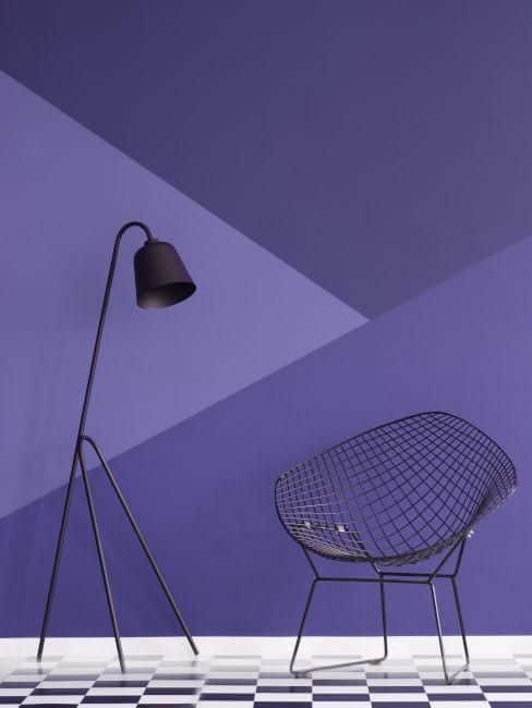 Modern room with geometric purple wall, black wire chair, and angled floor lamp on checkered floor.