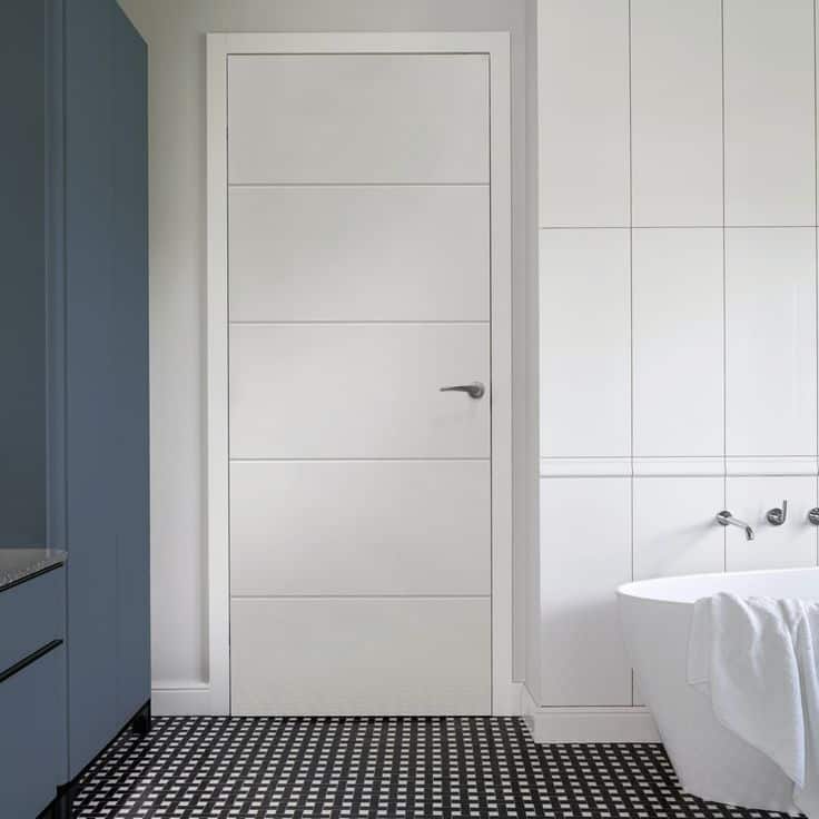 Modern bathroom with white door, freestanding tub, blue cabinet, and black and white tile flooring. Minimalist design.