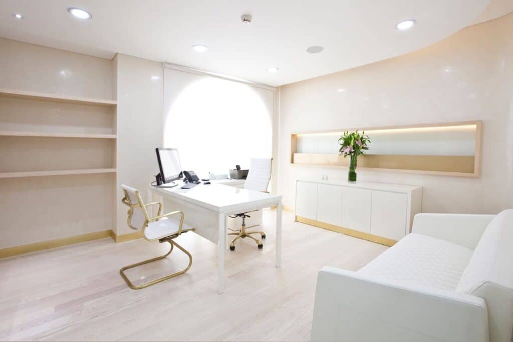 Bright, modern office interior with white furniture and natural lighting, featuring a desk, chair, and elegant decor.